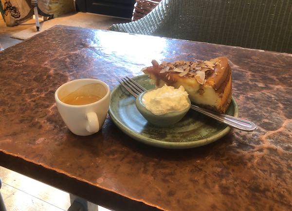 Cup of coffee and slice of cheesecake with whipped cream, sitting on a copper-topped table
