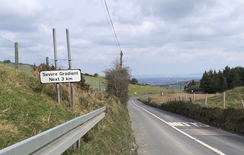 Road sign warning of "Severe Gradient Next 3km" next to road, Dublin visible in the background