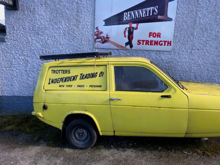 Yellow Robin Reliant three-wheeler van in the livery of Trotters independent Trading from the sit-com Only Fools And Horses, parked in front of a pebble-dashed pub wall in Ardcath