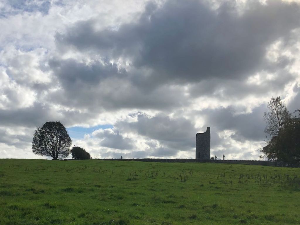Round tower silhouetted on a hillside under cloudy skies