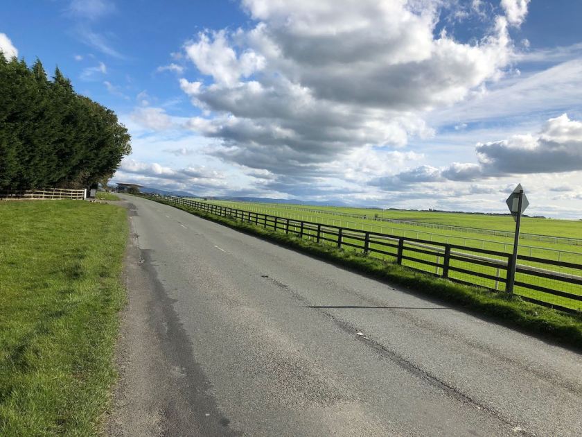 Road passing alongside a horse race course under partly clouded skies
