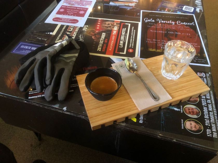 Gloves, cup of espresso and water on a glass-topped table with fliers for events under the glass