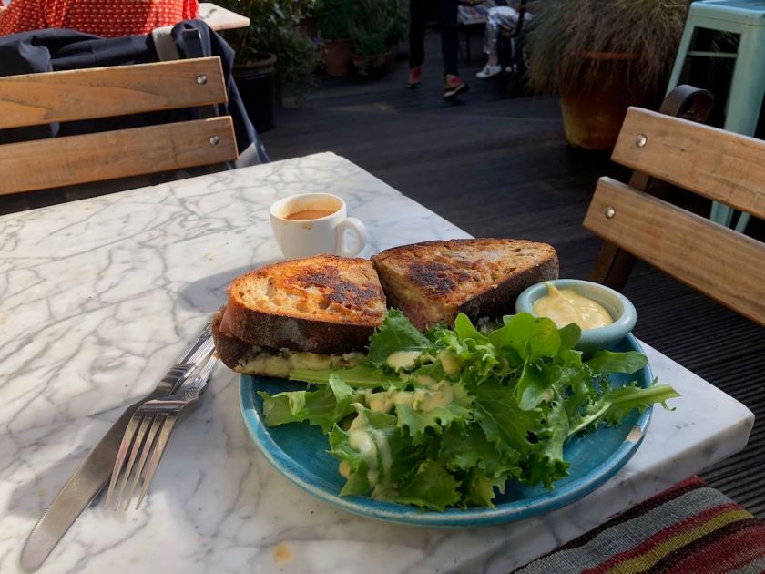 Toasted sandwich on plate with salad leaves and small pot of mustard dressing.