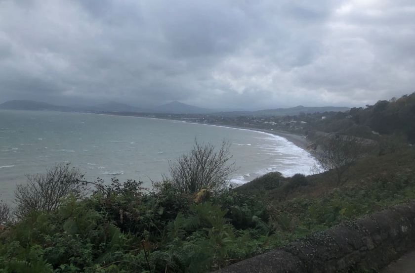 Coastline arcing around a bay under cloudy skies, headlands barely visible through the mist in the distance